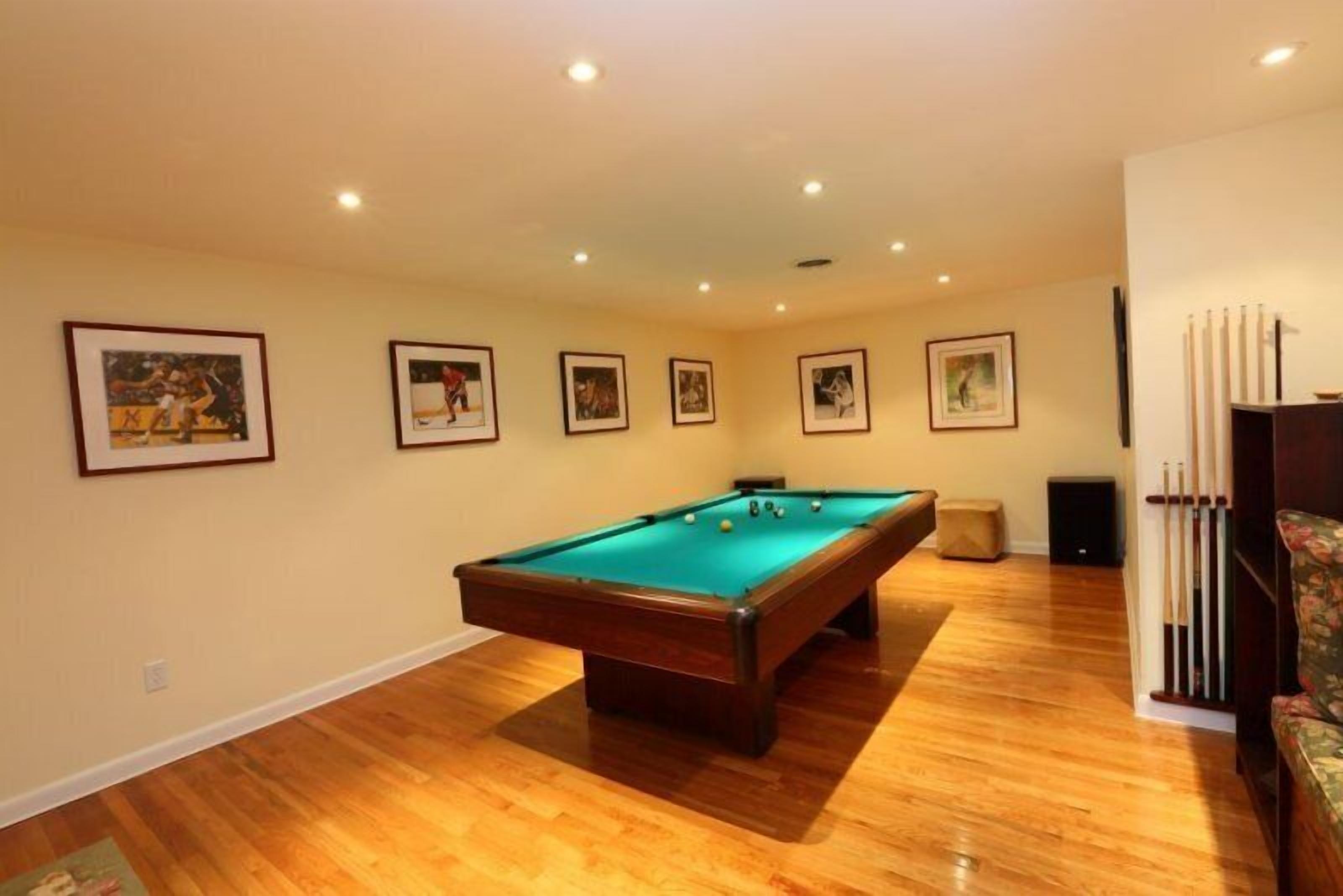 A pool table in a room with wooden flooring, framed pictures on the walls, and a speaker in the corner.