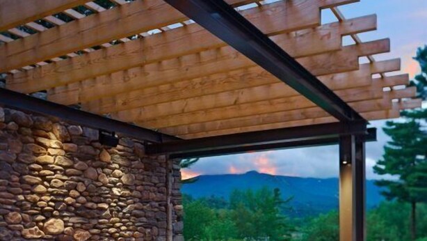 An outdoor seating area with a stone wall, a fire feature, and a view of mountains. - 627a_topnotch (Stowe)