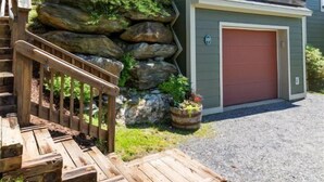 A two-story house with a red garage door, a wooden staircase leading to a deck, and a rock garden. - 608b_topnotch (Stowe)