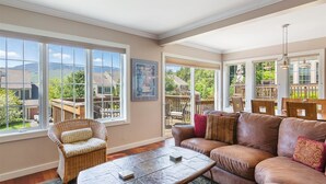 A spacious living room with large windows, a comfortable sofa, a wicker chair, and a stone coffee table. - 608b_topnotch (Stowe)