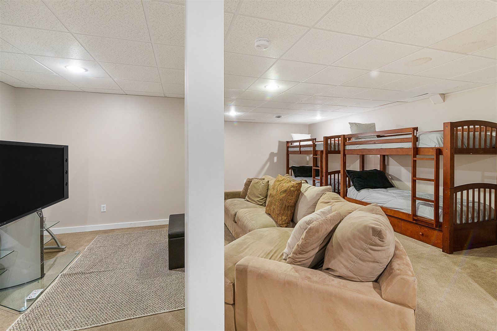 A room with bunk beds, a sofa, a TV, and a carpet.