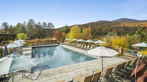 A rectangular pool with lounge chairs and umbrellas, surrounded by trees and a hilly landscape. - 608b_topnotch (Stowe)