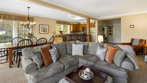A spacious living room with a sectional sofa, a dining area with a wooden table and chairs, and a kitchen in the background. - Family Friendly Overlook at Topnotch (Stowe)