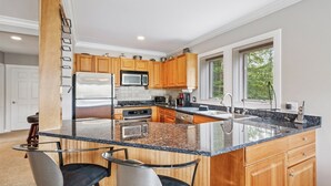A modern kitchen with granite countertops, stainless steel appliances, wooden cabinets, and a large window providing a view of greenery. - 3 Bears at Topnotch Resort & Spa (Stowe)