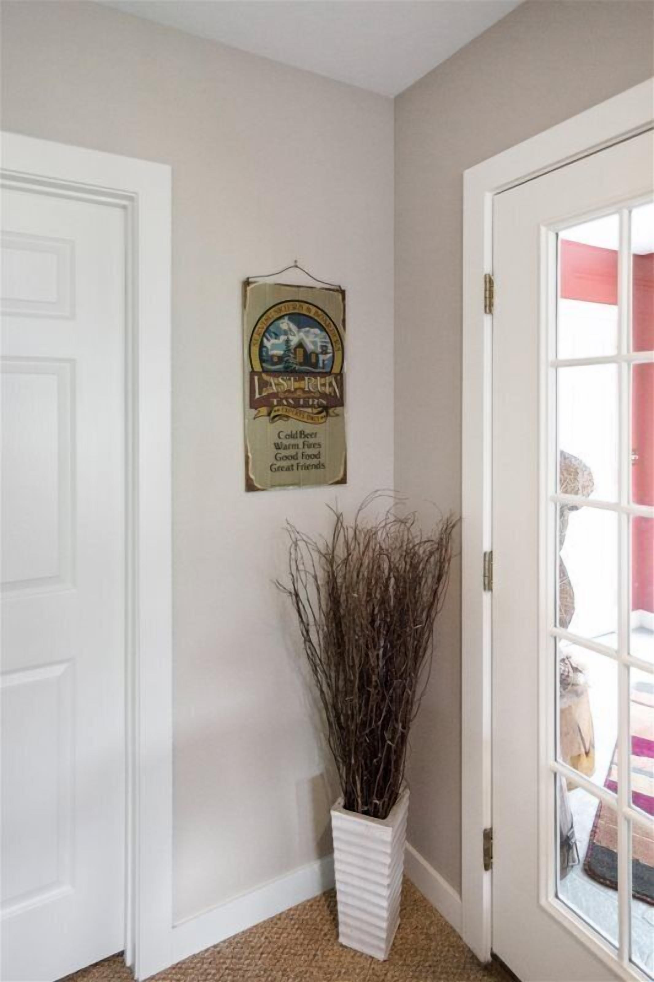 A hallway with a white door, a framed sign, and a white planter with branches.