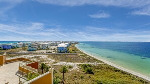 A coastal view with a beach, clear blue sky, and a pier extending into the ocean.