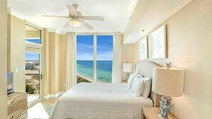 Une chambre d’hôtel avec un grand lit, un ventilateur de plafond, une vue sur l’océan et un balcon.