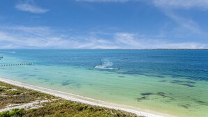 Une plage à l’eau turquoise et limpide, un rivage sablonneux et une jetée qui s’avance dans la mer.