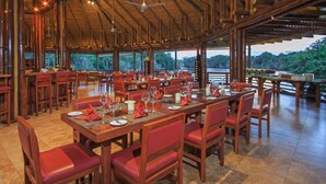 Un comedor amplio con mesas y sillas de madera, ventanas grandes que ofrecen vistas al exterior y un techo alto con vigas a la vista.