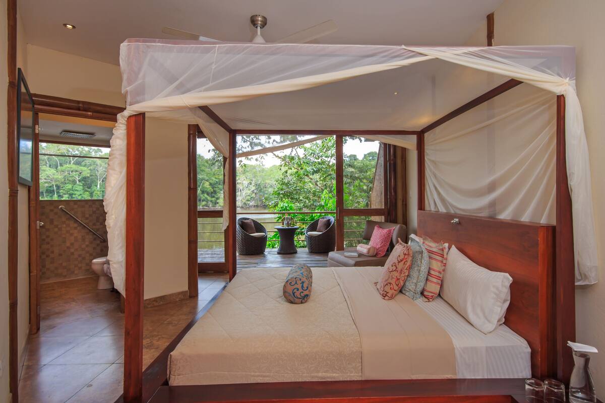Een slaapkamer met hemelbed, uitzicht op de omgeving en een balkon met zitplaatsen.