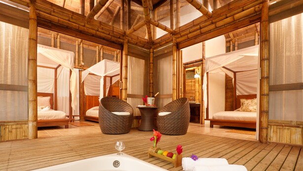 Habitación con decoración de bambú, una bañera grande, dos sillones de mimbre y dos camas con dosel.