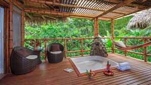 Una terraza de madera con un jacuzzi, dos sillas de mimbre y una hamaca.