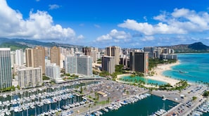 Un port de plaisance où sont amarrés de nombreux bateaux, entouré de grands immeubles et bordé d’une plage aux eaux turquoise et cristallines.