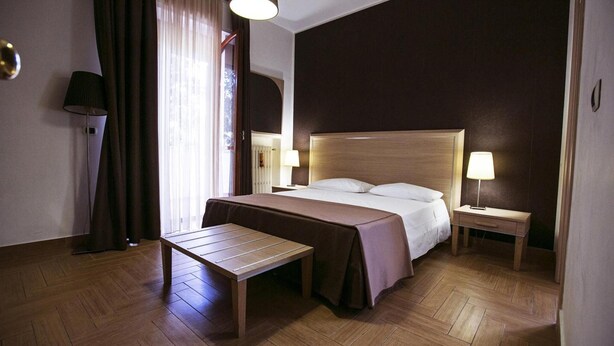 A hotel room with a large bed, bedside tables, a desk, and a window with curtains. - Villa del Mar (Bari)
