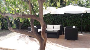An outdoor seating area with a sofa and chairs under a white umbrella, surrounded by greenery. - Villa del Mar (Bari)