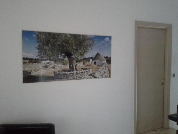 A room with a stone wall, a door, and a framed picture of a tree and a building. - Villa del Mar (Bari)