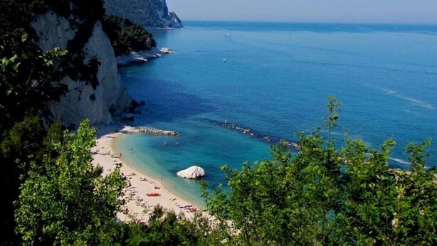 Un paisaje costero con una playa, mar azul cristalino y acantilados rocosos.