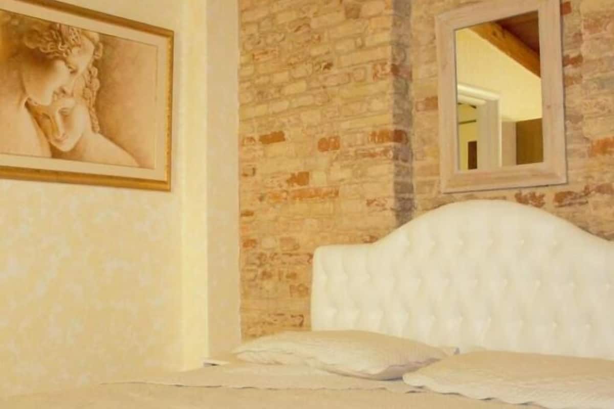 A bedroom with a brick wall, a framed portrait, and a white headboard.