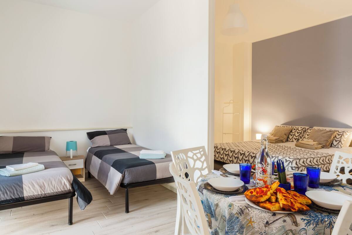 A room with two beds, a dining table with plates and a bottle, and a chair.