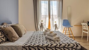 Un lit bien fait, avec une literie à motifs, une chaise bleue et un bureau agrémenté d’un miroir.