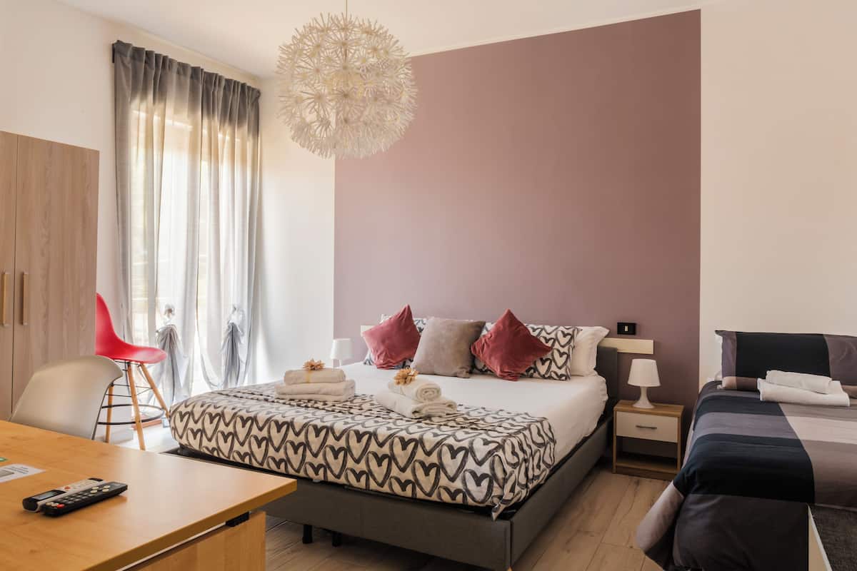 A modern hotel room with a bed, bedside tables, a desk, and a chair.