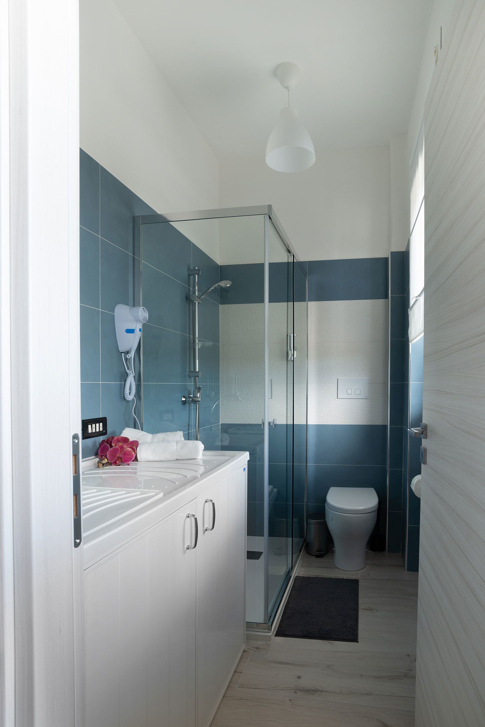A modern bathroom with a glass shower enclosure, a white sink, and a blue-tiled wall.