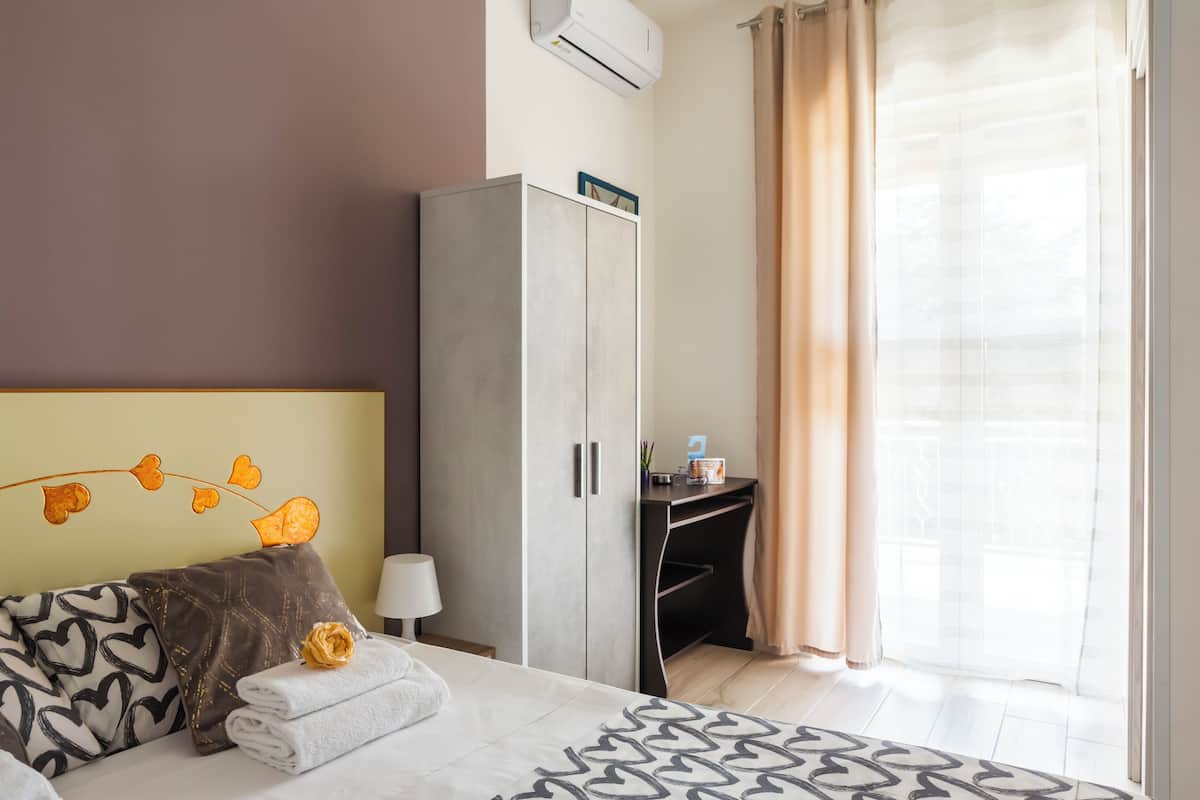 A hotel room with a bed, a wardrobe, a desk, and a window with curtains.