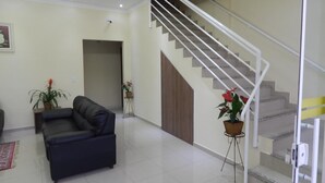 A living room with a dark sofa, a staircase, and potted plants.