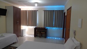 A hotel room with a bed, a desk, and a chair. There is a wardrobe and a television on the wall.