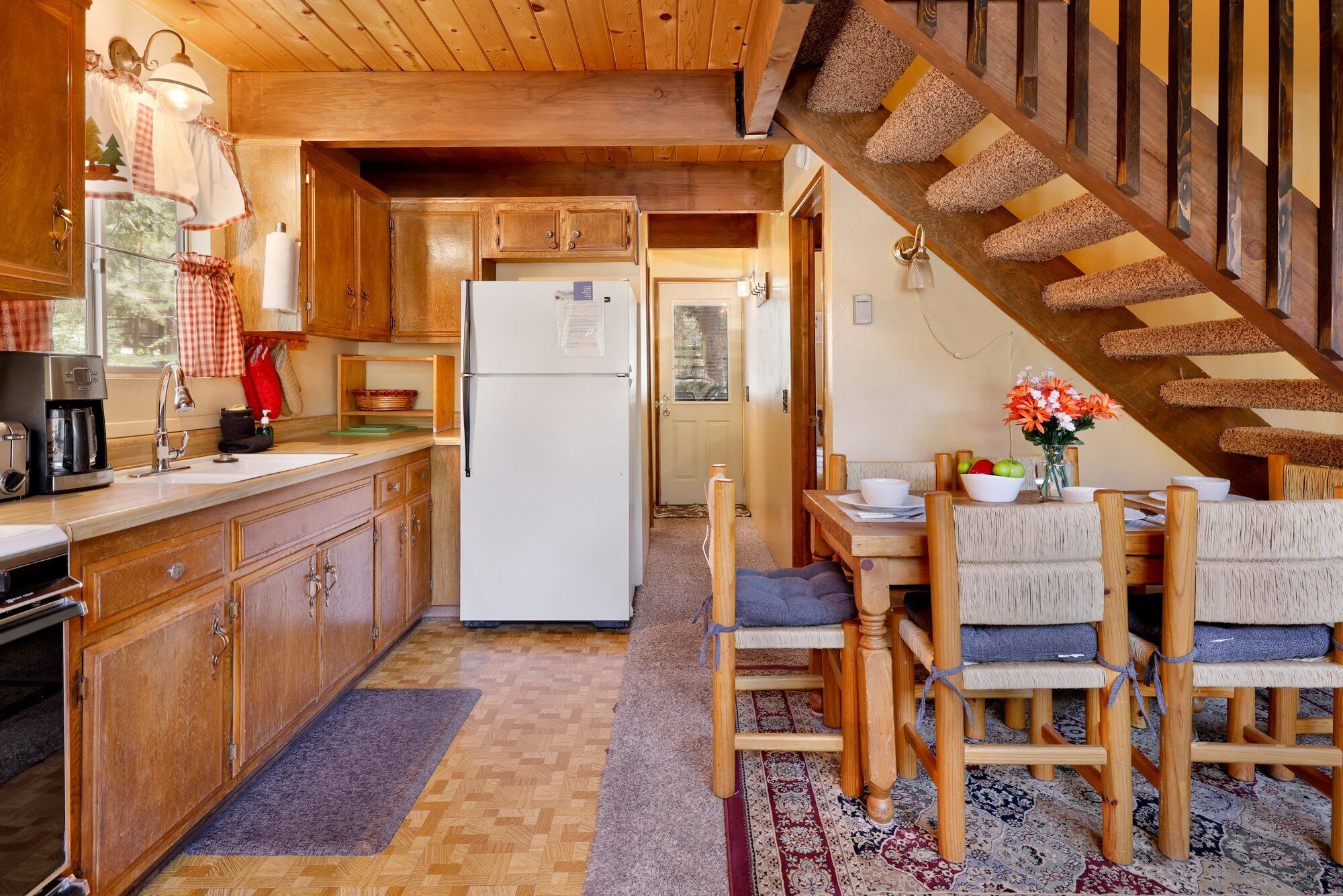 A cozy kitchen with wooden cabinets, a white refrigerator, and a dining area with a wooden table and chairs.