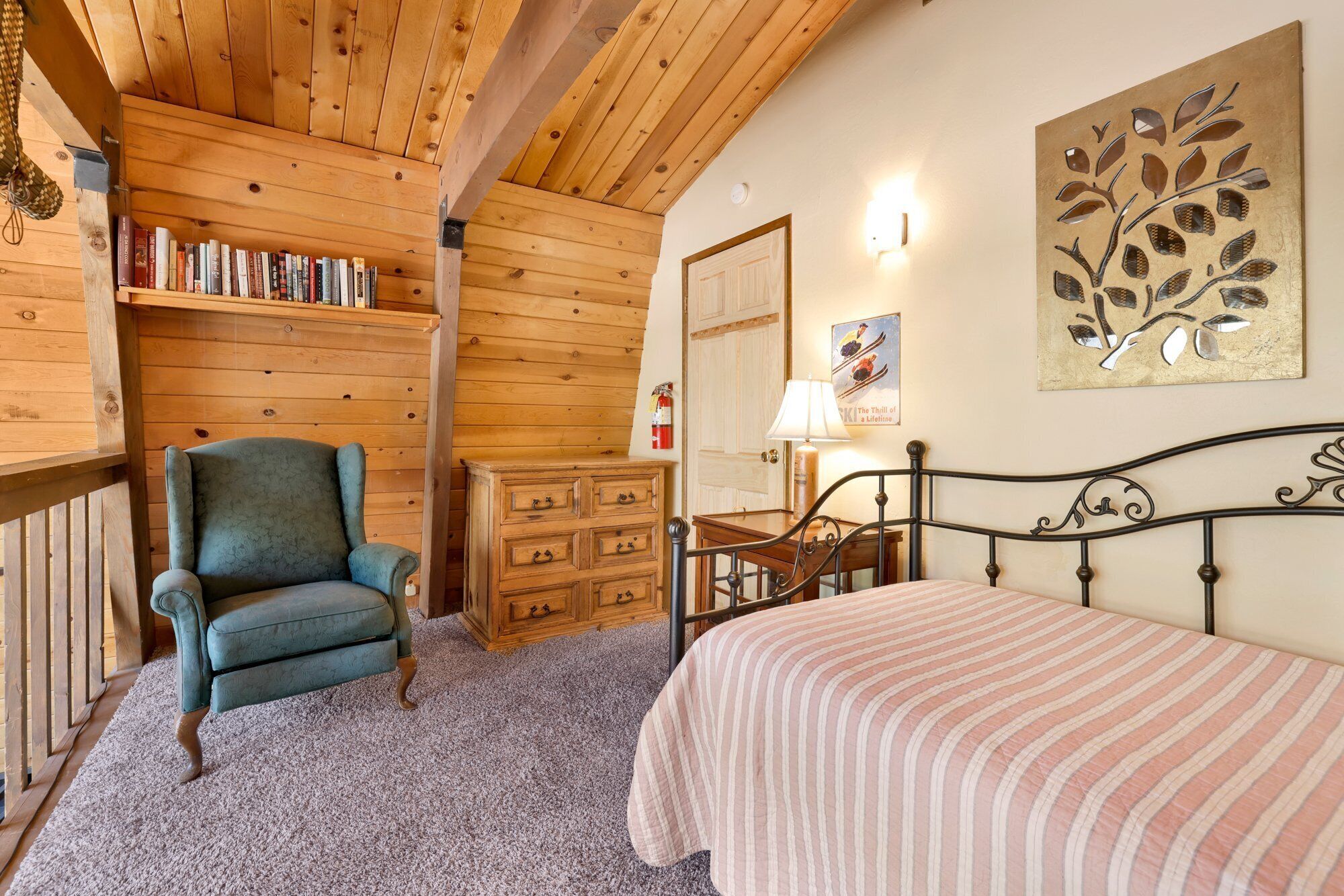 Ein gemütliches Zimmer mit einem Bett, einem Sessel, einer Holzkommode und einem Bücherregal.