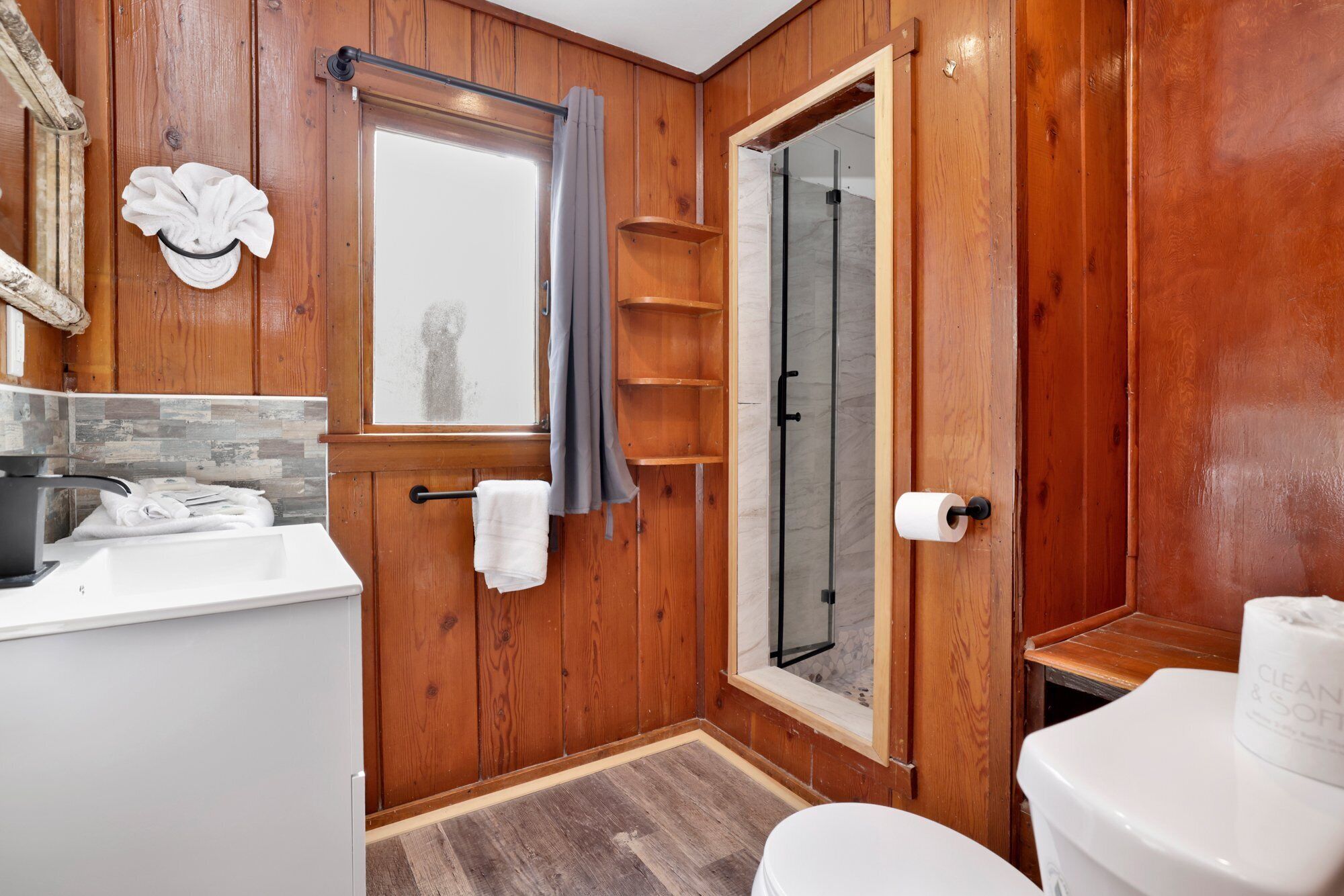A wooden bathroom with a shower, toilet, and sink.