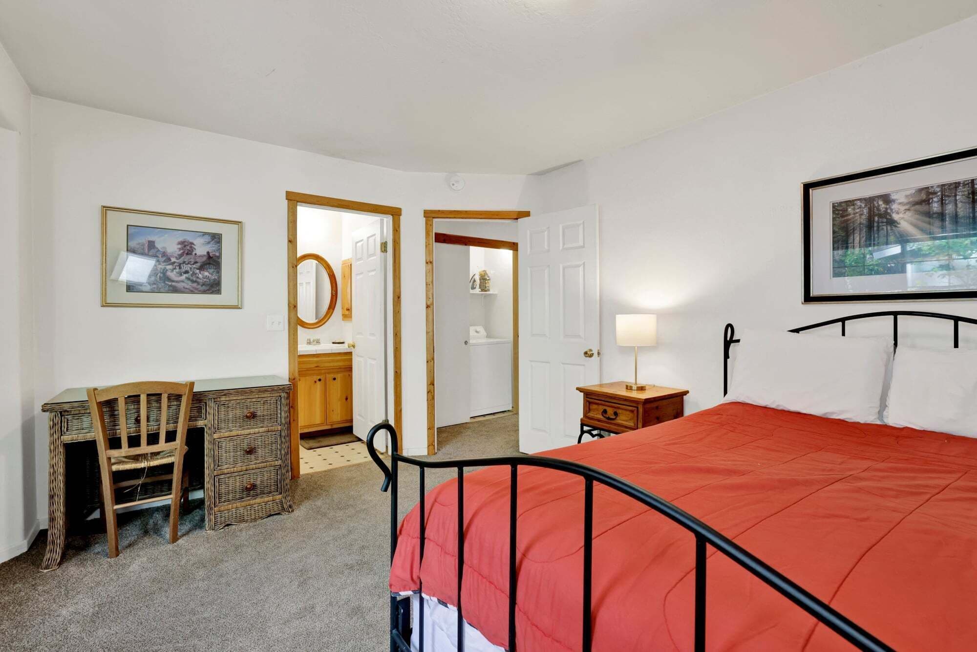 A bedroom with a bed, a desk, a chair, a dresser, and a door leading to a bathroom.