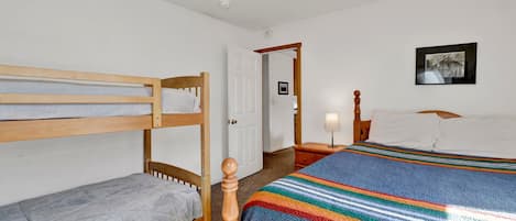 A room with bunk beds, a single bed, a bedside table with a lamp, and a framed picture on the wall.