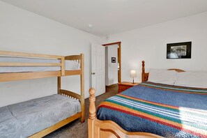 A room with bunk beds, a single bed, a bedside table with a lamp, and a framed picture on the wall.