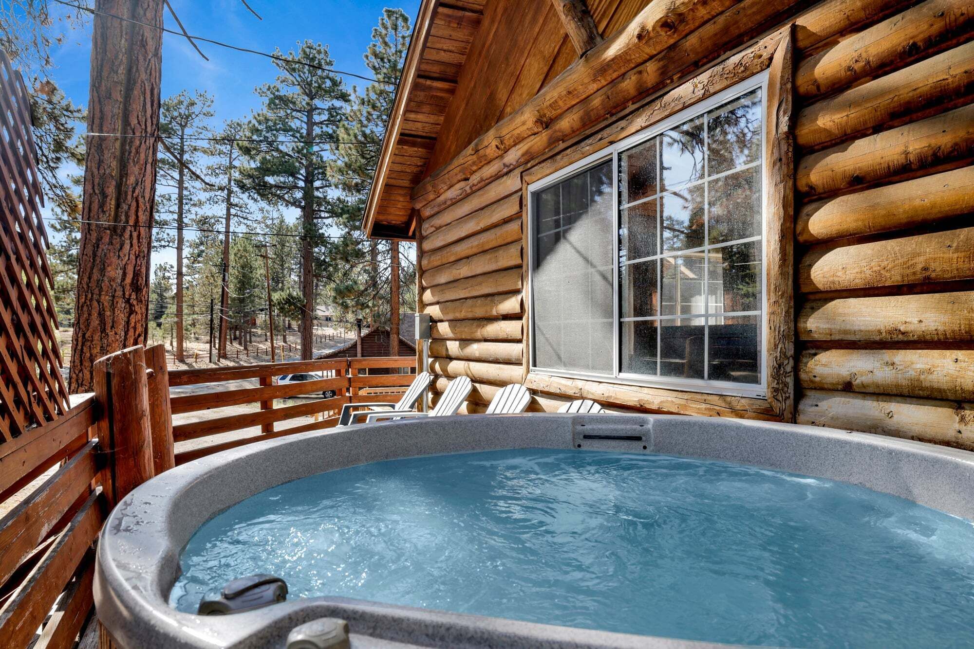 A wooden cabin with a hot tub on a deck, surrounded by trees.