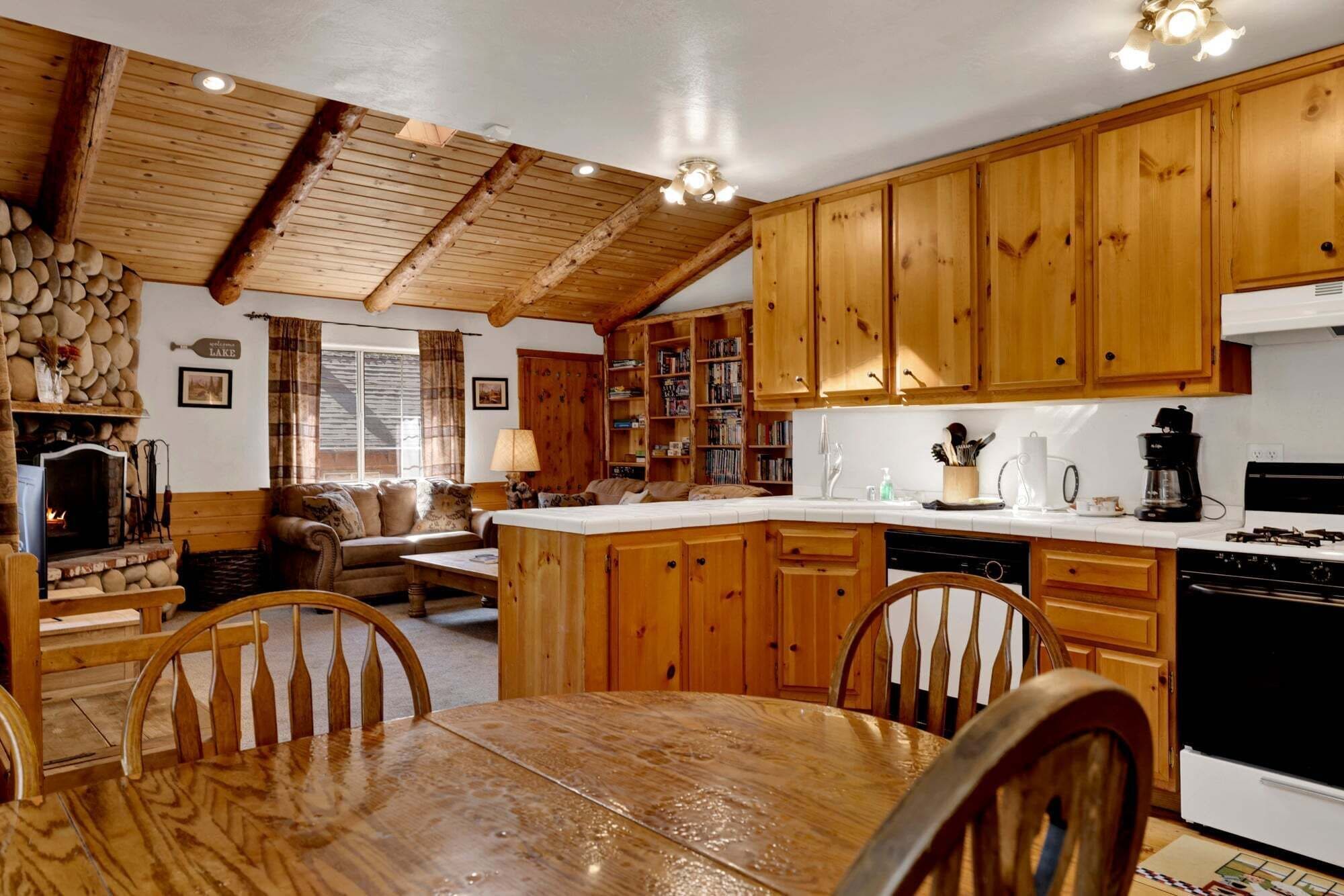 A rustic kitchen with wooden cabinets, a stone fireplace, and a dining area with a wooden table and chairs.