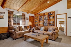 A cozy living room with wooden furniture, a bookshelf, and a window with curtains. - Forest Treehouse # 1473 (Big Bear Lake)