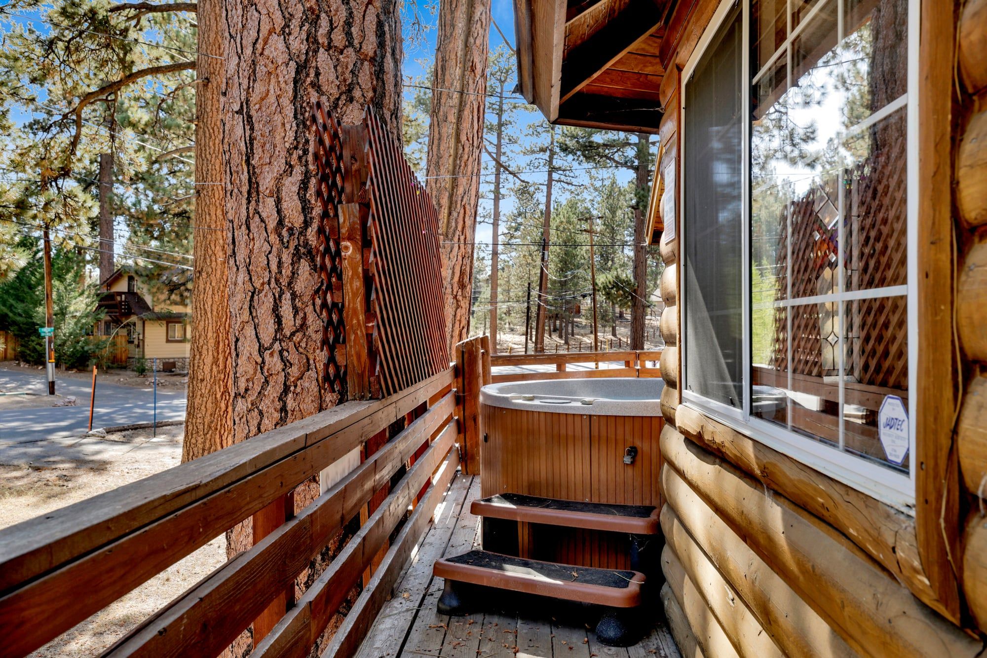 A wooden cabin with a hot tub, wooden deck, and a large tree trunk.