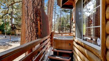 A wooden cabin with a hot tub, wooden deck, and a large tree trunk.