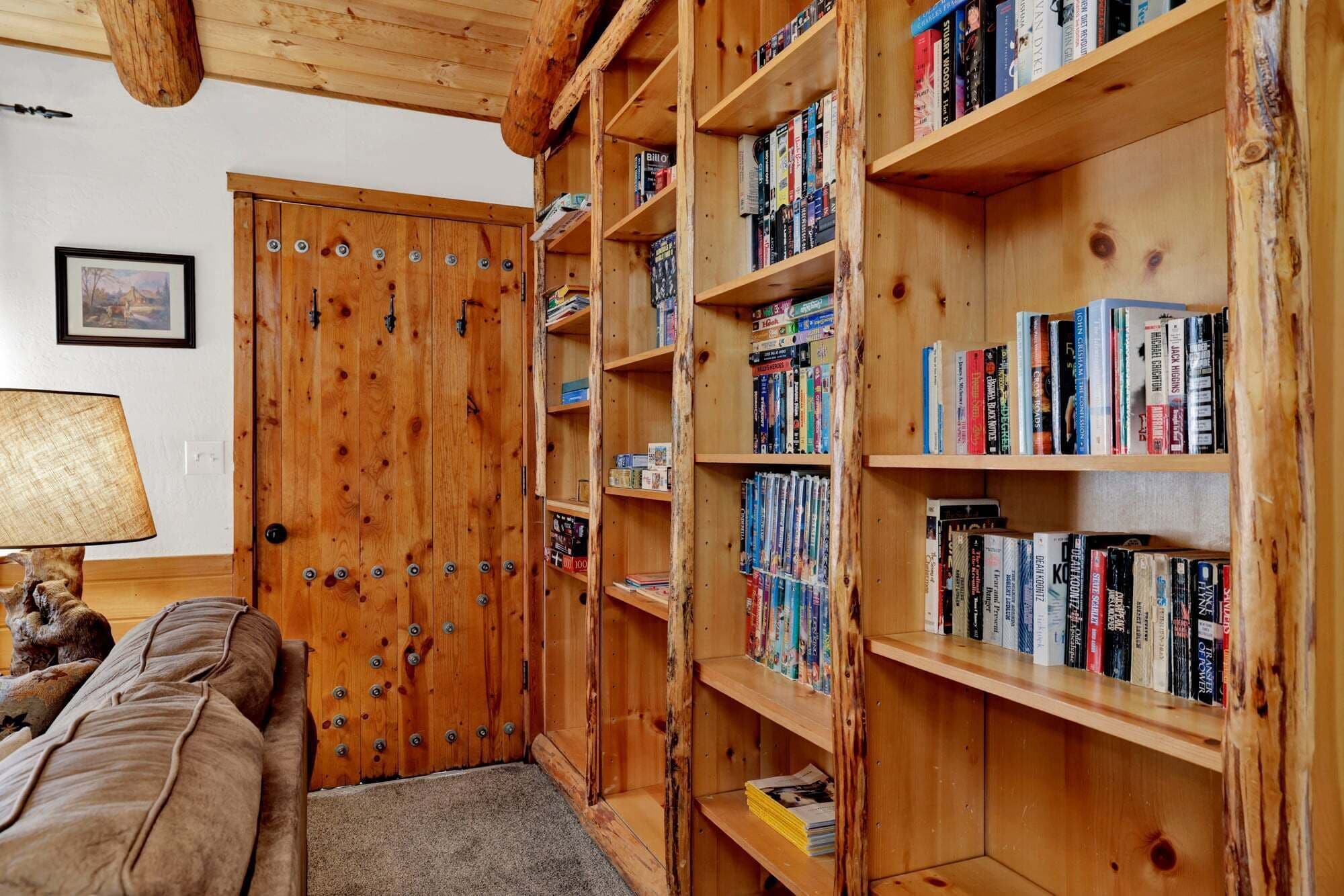 A cozy room with a wooden bookshelf filled with books, a wooden door, and a lamp on a table.