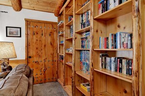 A cozy room with a wooden bookshelf filled with books, a wooden door, and a lamp on a table. - Forest Treehouse # 1473 (Big Bear Lake)