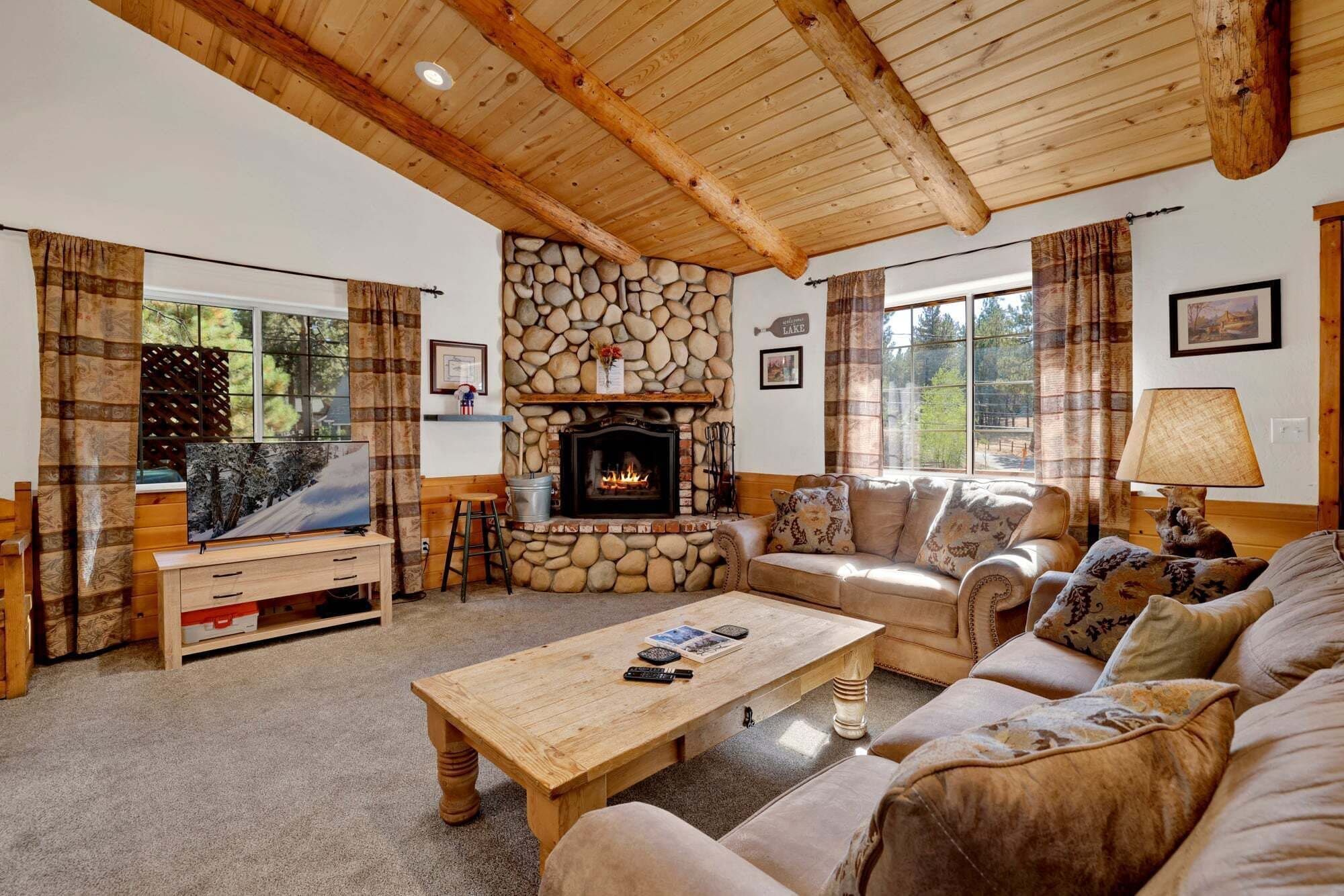 A cozy living room with a stone fireplace, a sofa set, a coffee table, and a television.