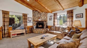 A cozy living room with a stone fireplace, a sofa set, a coffee table, and a television.