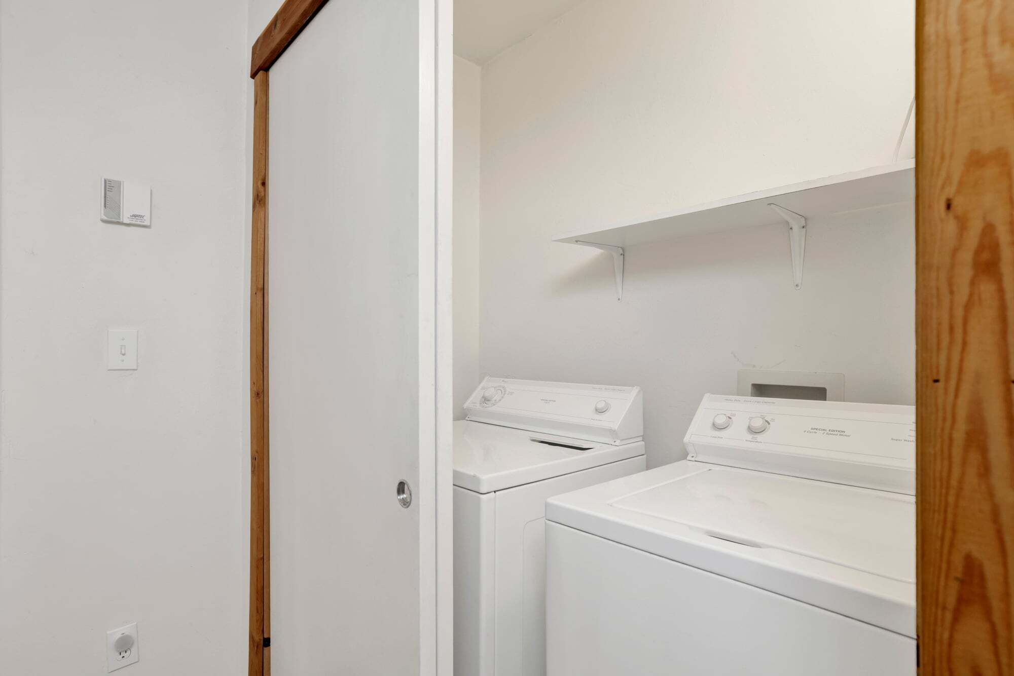 A laundry room with two white washers and dryers, wooden door frame, and a white wall.