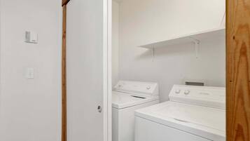 A laundry room with two white washers and dryers, wooden door frame, and a white wall.