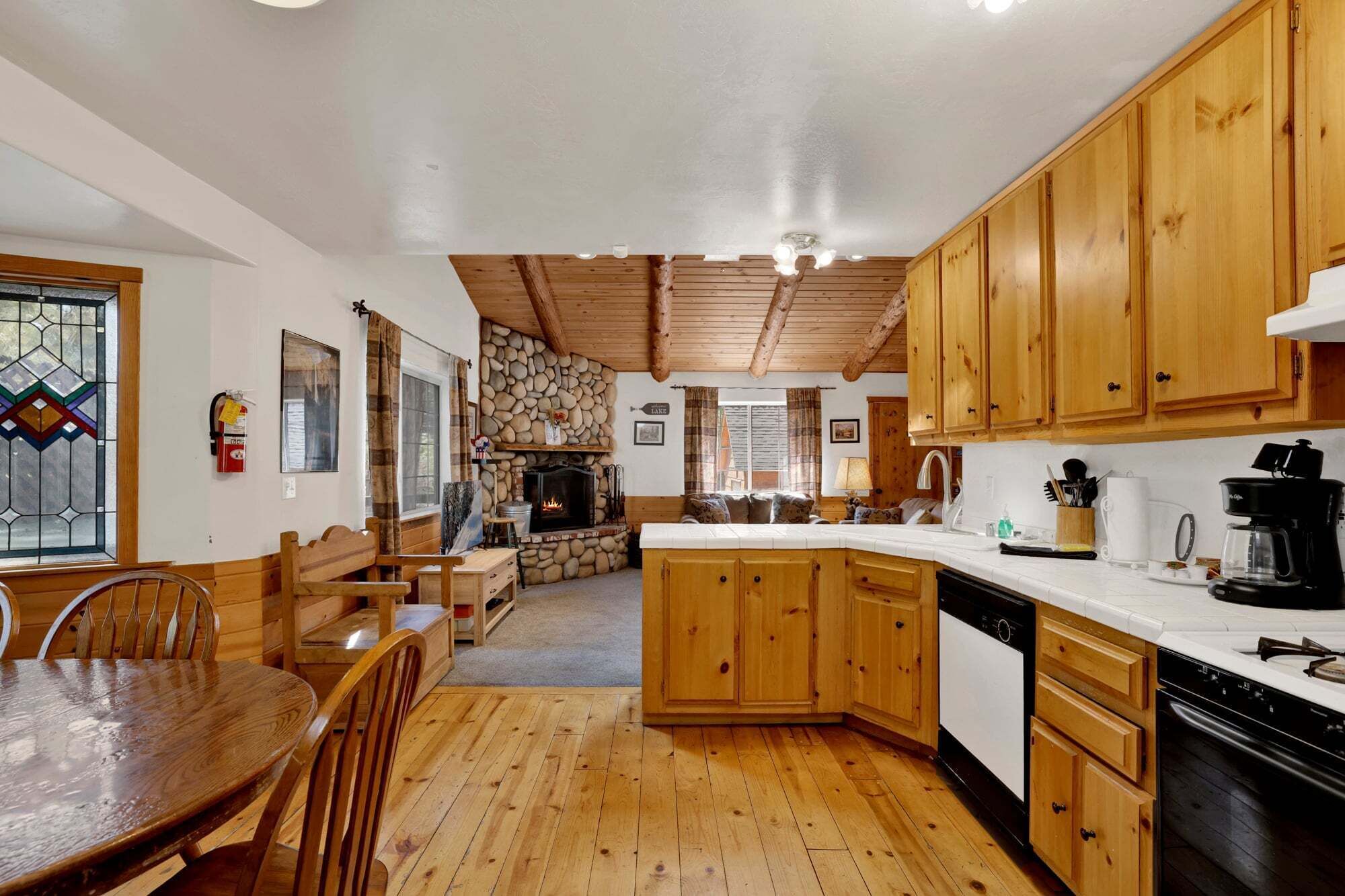 A cozy kitchen with wooden cabinets, a stone fireplace, and a dining area with a wooden table and chairs.