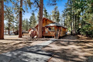 A rustic log cabin with a wooden deck and a staircase leading to the entrance. - Forest Treehouse # 1473 (Big Bear Lake)