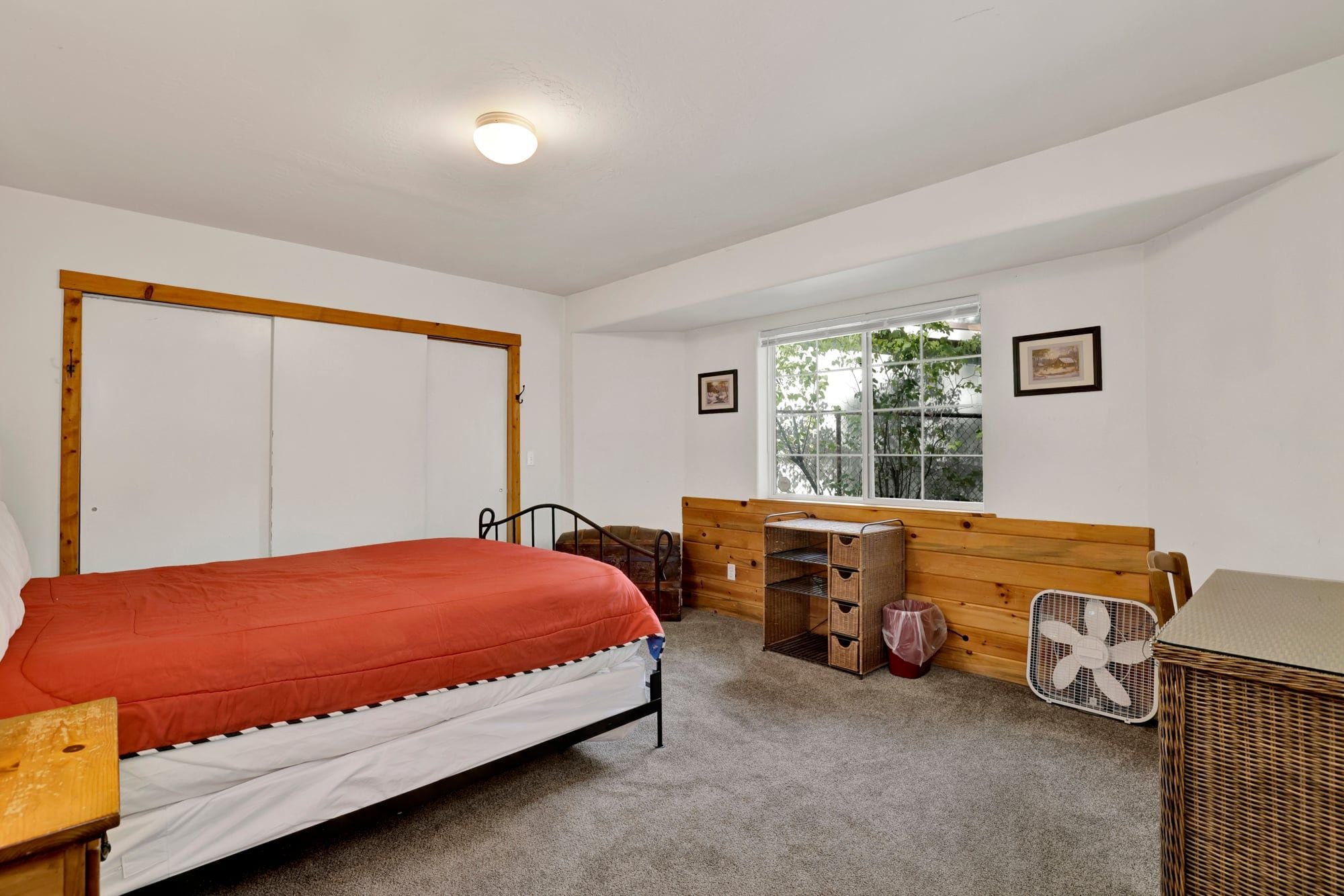 A bedroom with a bed, a wooden bench, a window, and a fan.