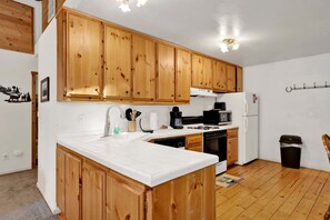 A kitchen with wooden cabinets, a white countertop, a sink, a stove, a microwave, and a refrigerator. - Forest Treehouse # 1473 (Big Bear Lake)